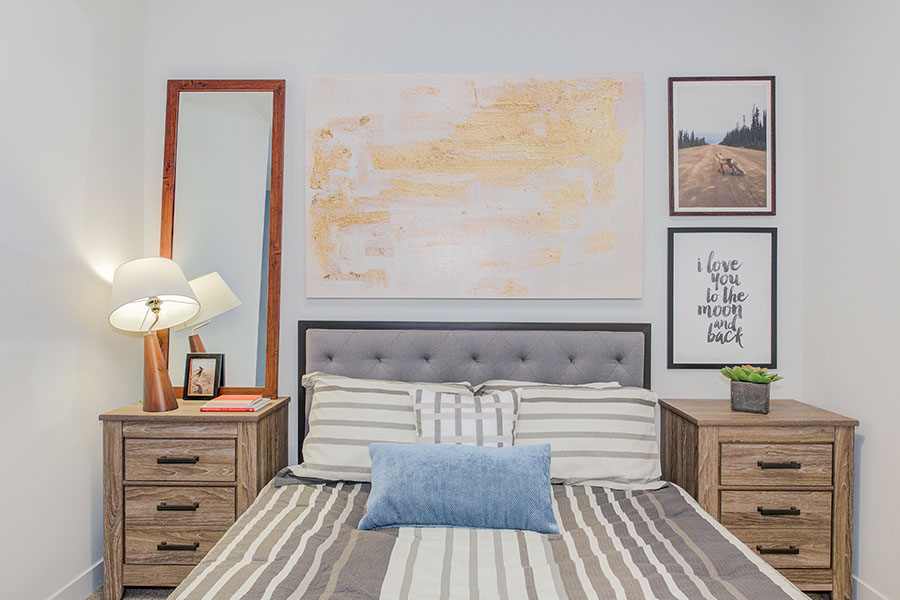 A gray bed in a white room with art on the wall